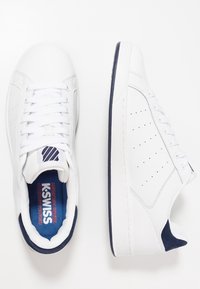 Bílé šněrovací tenisky s hladkým koženým svrškem, námořnickými akcenty na patě a jazyku, perforovanými boky a strukturovanou podrážkou.
