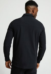 Melnas garām piedurknēm krekls ar strukturētu apkakli, pogu aprocēm un gludu auduma apdari. Iespējas plecu šuves un aizmugurējā yoke.