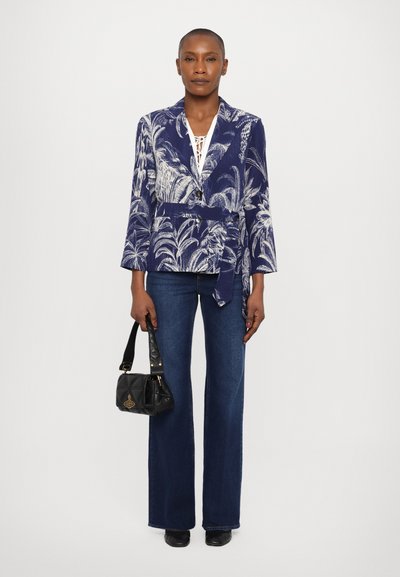 Jūras zila ziedu žakete ar baltu palmu rakstu, ar jostas sasienamo daļu, apvienota ar flared tumšo džinsu biksēm un mazu melnu rokassomu.