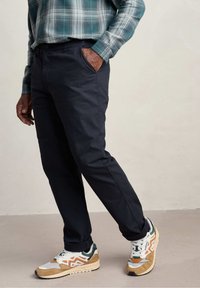 Marineblauwe chino's met een slim fit, voorzien van twee zijzakken en een gladde stof. Gepaard met sportieve, multikleurige sneakers voor contrast.