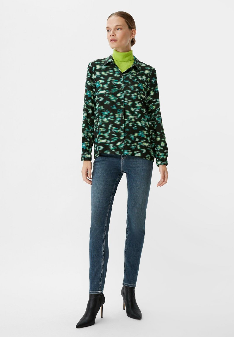 Black and green patterned blouse with long sleeves, paired with blue skinny jeans and black pointed ankle boots. Smooth fabric texture.