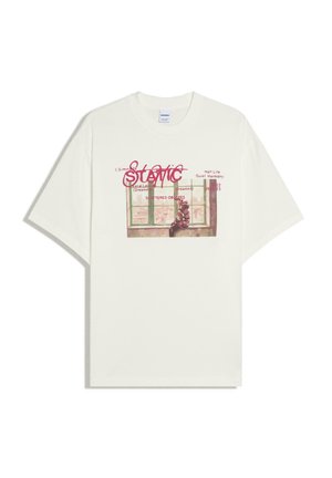 Maglietta bianca con una grafica di una persona seduta vicino a una finestra, sovrapposta a un testo rosso che include la parola "Static" e frasi più piccole.