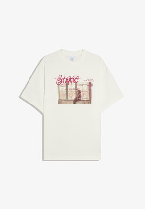 T-shirt blanc avec un graphisme d'une personne assise près d'une fenêtre, surmonté de texte rouge comprenant le mot « Static » et des phrases plus petites.