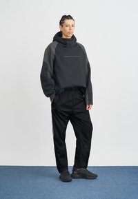 Must mustaga kootiga dress ja hallidega aktsentidega, esipaneelil logo. Kombineeritud mustade kitsaste pükste ja tumedate sportlike kingadega. Lame pinna taust.