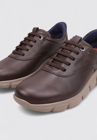 Zapatos de cuero marrón con cordones, punta redondeada, superficie texturizada y suela acolchada beige. El interior presenta acentos en azul marino.