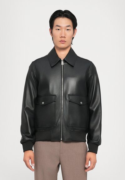 Chaqueta bomber de cuero negro con cuello tipo solapa, cierre frontal con cremallera y dos bolsillos en el pecho; tiene puños acanalados y un acabado liso.