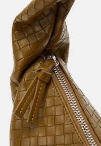 Bolso marrón de cuero tejido con superficie texturizada, cremallera prominente con herrajes plateados y detalle anudado en la parte superior.