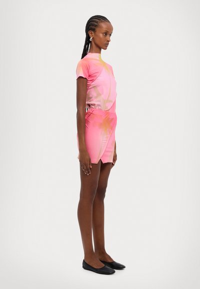 Rosa Kurzarmkleid mit taillierter Silhouette, das ein Farbverlaufdesign und einen asymmetrischen Saum aufweist. Glattes Material; Modell trägt schwarze Ballerinas.