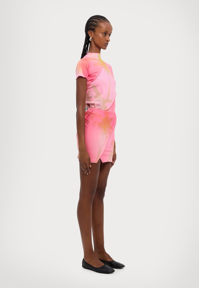 Pink short-sleeve dress with a fitted silhouette, featuring a gradient design and an asymmetrical hem. Smooth fabric; model wearing black flats.