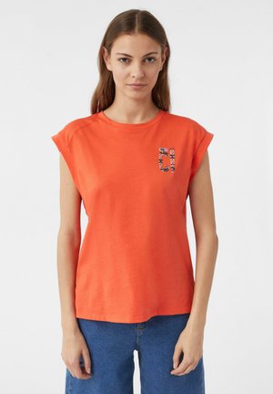 Pomarańczowy t-shirt bawełniany z krótkimi, podwiniętymi rękawami oraz graficznym wzorem kwiatowym na lewej piersi. Design ma luźny fason.