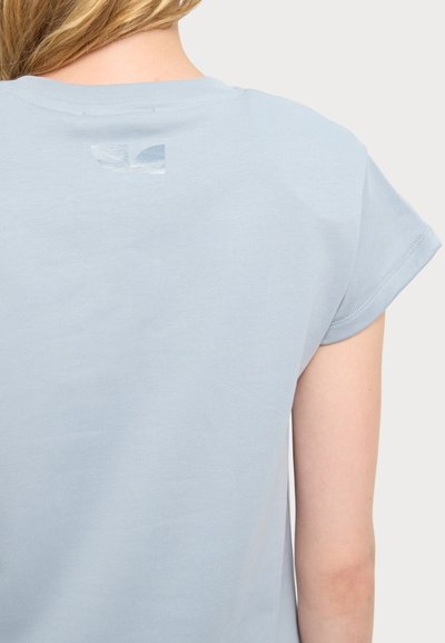 Camiseta de manga corta color azul claro con cuello redondo. Presenta un pequeño detalle de logo en la parte posterior del cuello. Tejido suave de algodón con ligera textura.