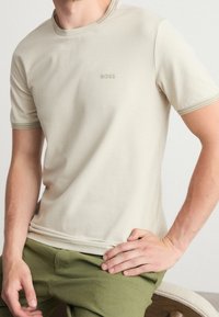 T-shirt beige a maniche corte con colletto e polsini a coste, caratterizzato da un discreto logo "BOSS" sul petto. Tessuto morbido e liscio.