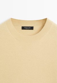 Beige knitted sweater with a rounded crew neck, ribbed collar, and subtle texture. Label reads "Massimo Dutti," indicating brand origin.