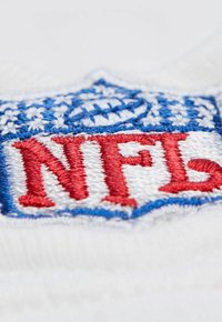 Nahaufnahme eines weißen Stoffes mit besticktem blauen und roten NFL-Logo, das einen Fußball und stilisierte Buchstaben auf strukturiertem Material zeigt.