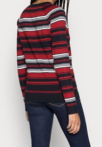 Suéter de manga larga con rayas verticales en rojo, negro y blanco. Material de punto suave con cuello redondo y diseño ajustado.