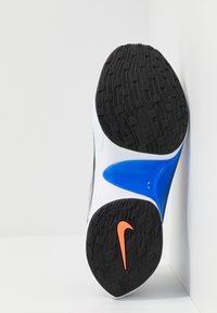 Nike Sportschuh mit schwarzer Gummilaufsohle, weißem Obermaterial, glänzend blauem Zwischensohlenbereich und orangefarbenem Logo. Verfügt über ein strukturiertes Profil für besseren Halt.