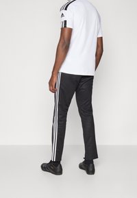 Conjunto deportivo masculino que incluye una camiseta blanca de manga corta y pantalones negros con tres rayas blancas a los lados, combinados con zapatillas negras.