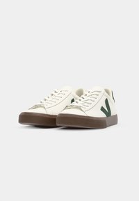 White sneakers with green accents and a brown rubber sole. Features laces, rounded toe, leather upper, and side logo detail.