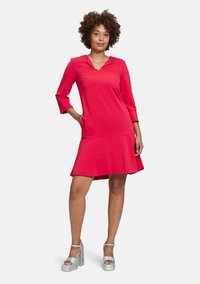 Rotes knielanges Kleid mit Kragen und Dreiviertelärmeln. Der Saum ist leicht ausgestellt. Kombiniert mit silbernen Plateausandalen.