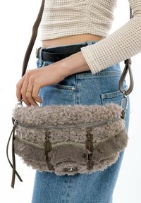 Borsa grigia con texture, caratterizzata da un esterno morbido e peloso, decorata con una cerniera metallica e dettagli in pelle. Inclusa una tracolla regolabile.