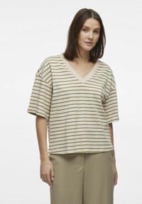 Beżowa koszulka V-neck z poziomymi zielonymi paskami, krótki rękaw i luźny krój. Miękka tkanina o gładkiej fakturze, zestawiona z khaki spodniami.