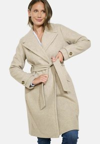 Bežinė vilnos mišinuko palaidinė su diržu, iškirpte ir sagomis. Lygi tekstūra, vidutinio ilgio iki šlaunų ir pritaikytas dizainas.