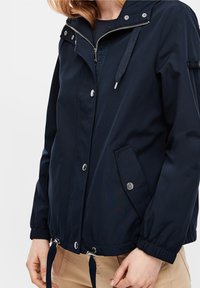 Chaqueta azul marino con herrajes plateados, cierre de cremallera y botones a presión. Cuenta con puños elásticos y dobladillo con cordón para un ajuste ajustable.