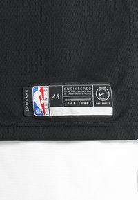 Czarny materiał koszulki do koszykówki z teksturą siateczkową. Charakteryzuje się metką z logo NBA, napisem „SWINGMAN”, rozmiar 44 oraz brandingiem NikeConnect. Biały akcent na dole.