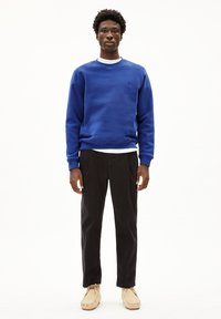 Blauer Pullover mit Rundhalsausschnitt, langen Ärmeln und strukturiertem Stoff. Kombiniert mit schwarzen Hosen und beigen Mokassins.