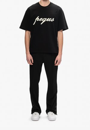 Black oversized cotton t-shirt with white "pegus" graphic, paired with black trousers and white sneakers featuring button accents.