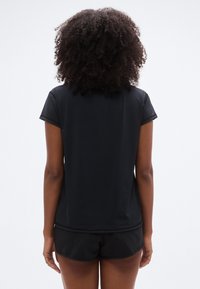 Μαύρο αθλητικό τοπ με κοντά μανίκια, απαλής υφής και στρογγυλή λαιμόκοψη, σε συνδυασμό με μαύρο αθλητικό σορτς. Καθαρός, απλός σχεδιασμός.