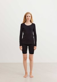 Maglietta nera a maniche lunghe e pantaloni da biker neri realizzati in morbido tessuto elasticizzato. La maglietta presenta un girocollo e una silhouette aderente.