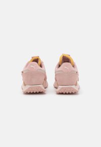 Baskets Puma en daim rose avec talon coussiné, accents jaunes et semelle extérieure à traction prononcée ; design épuré avec détail du logo.
