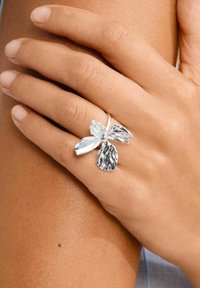 Anello d'argento a forma di fiore con petali testurizzati e un centro liscio, mostrato su una mano abbronzata su uno sfondo neutro.
