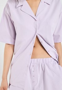 Light lavender two-piece set featuring short-sleeve button-up top with a chest pocket and elastic waist shorts with button details.