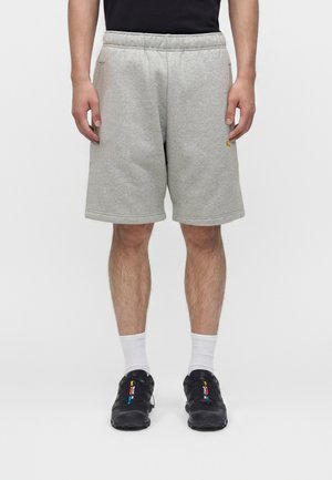 Mand iført lysegrå knælange shorts, hvide crew-sokker og sorte sneakers med farverige detaljer, stående mod en ensfarvet hvid baggrund.