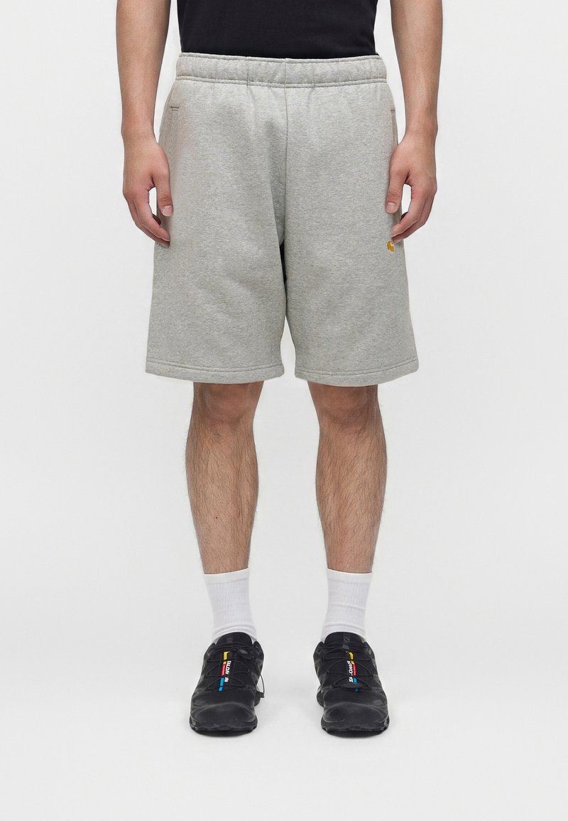 Mann trägt hellgraue knielange Shorts, weiße Crew-Socken und schwarze Sneakers mit bunten Details, steht vor einem einfarbigen weißen Hintergrund.
