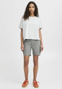 T-shirt grise coupée avec des manches courtes, assortie à un short cargo gris avec des poches latérales. Des baskets rouges avec des accents blancs complètent le look.