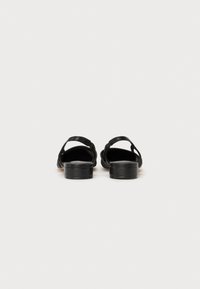 Sandales en cuir noir avec un petit talon bloc et deux brides croisées. Texture lisse, design minimal, dos ouvert pour un enfilage facile.