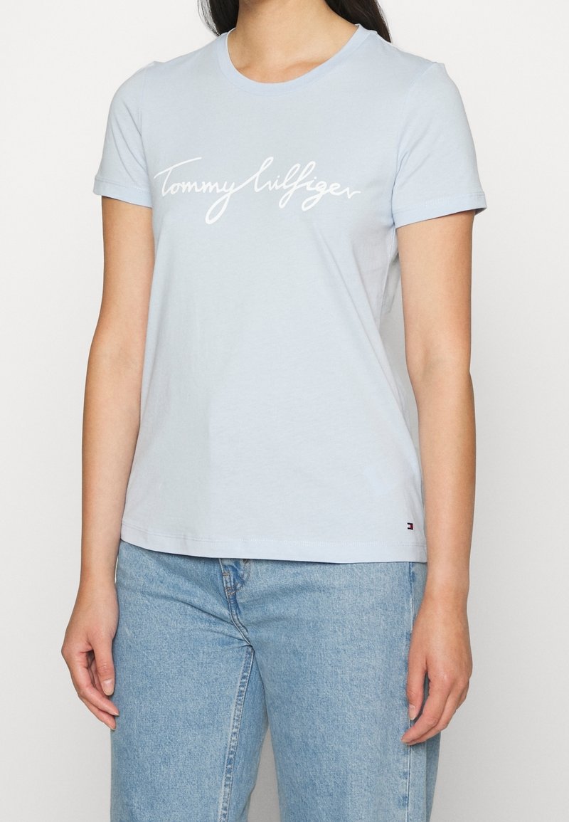 Jasnoniebieska bawełniana koszulka z krótkim rękawem, okrągłym dekoltem, z białym napisem "Tommy Hilfiger" na przodzie. Swobodny krój.