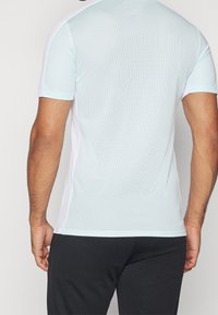 Light blue short-sleeve active shirt with a textured mesh fabric, contrasting white side panels, and a fitted design, suitable for sports.