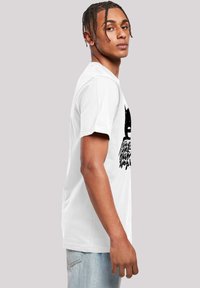 White cotton T-shirt featuring a graphic with a black design, depicting a character and text, with short sleeves and a crew neckline.