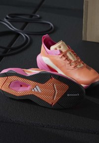 Paire de chaussures de course roses et orange sur un sol noir, une semelle visible avec les logos Adidas et Continental.