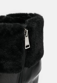 Černé kotníkové boty s huňatým černým lemem, hladkým koženým tělem, zipovým uzávěrem se stříbrnými doplňky a mírným podpatkem.