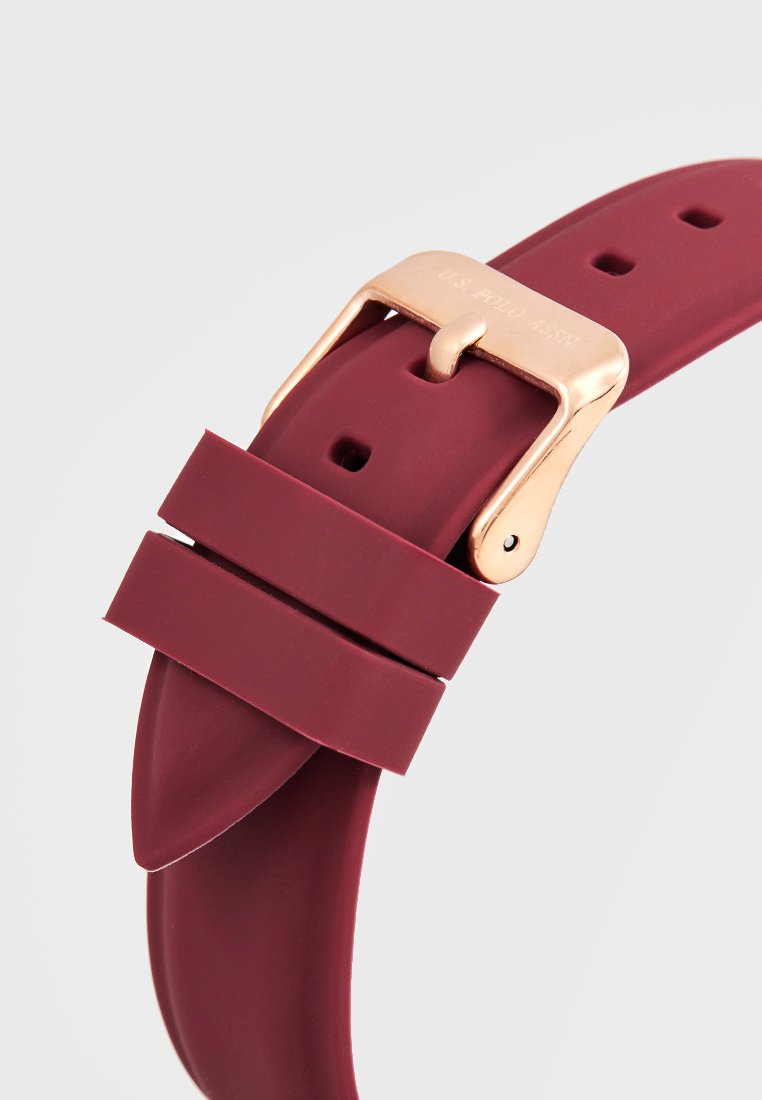 Rotes Silikon-Uhrenarmband mit einer goldfarbenen Metallschnalle und zwei Halteschlaufen. Es hat eine glatte Oberfläche und mehrere Einstelllöcher.