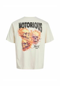 Krémové bavlnené tričko s grafikou troch lebiek obklopených plameňmi. Hrubé čierne písmo znie "NOTORIOUS."
