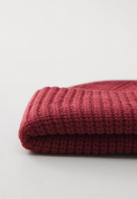 Sciarpa di maglia piegata di un rosso profondo con texture a coste su una superficie bianca.