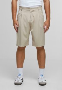 Beige shorts gemaakt van lichtgewicht stof met een geplooid voorkant, voorzien van een knoopsluiting en een relaxte pasvorm, gecombineerd met witte sneakers.
