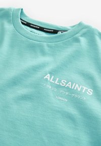 Mintgrön t-shirt i bomull med rund halsringning och vit text, inklusive "ALLSAINTS" och "LONDON" på framsidan.