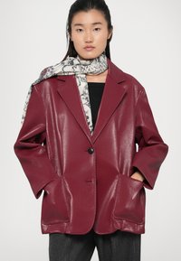 Blazer in ecopelle bordeaux con una finitura testurizzata, caratterizzato da un colletto a revers, un singolo bottone nero e grandi tasche frontali.